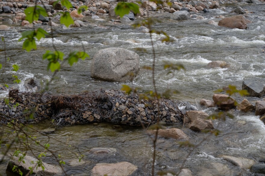 Several small rocks tied together by netting lay in a river as rater rushes past.