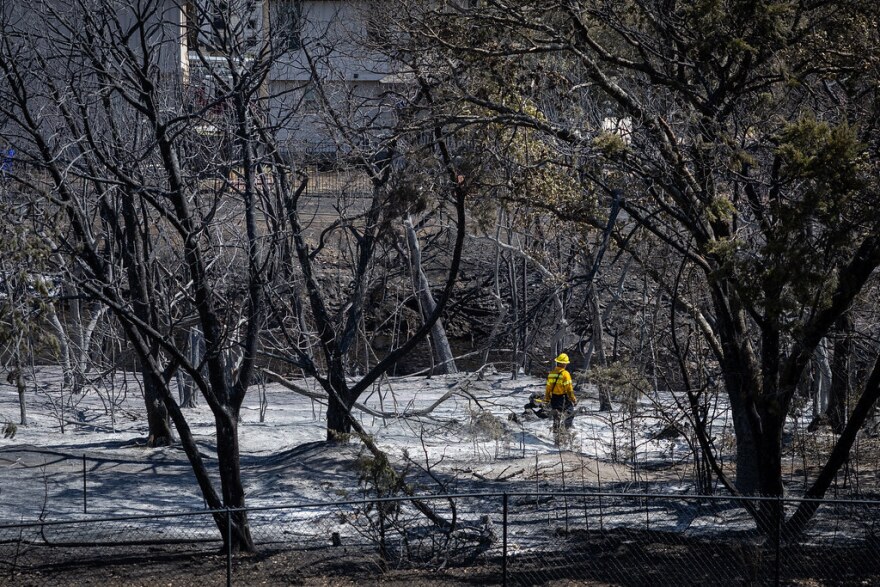 A firefighter walks across scorched, smoking ground and trees behind the Bexley at Silverado apartments on Aug. 9, 2023, in Cedar Park. A wildfire developed in the area the night before, triggering evacuations and destroying one apartment building and damaging three others.<br/>