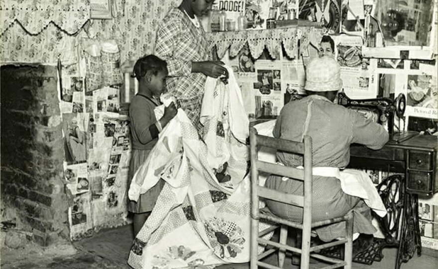 In this 1937 image by Farm Security Administration photographer Arthur Rothstein, Gee's Bend quilter Jorena Pettway sews a quilt as two young girls hold the fabric for her.