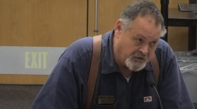 A bearded man speaks into a microphone.