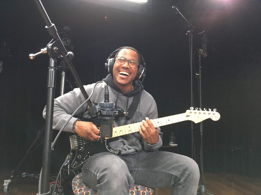 Detroit artist Cozine Welch playing the electric guitar. He is seated with a microphone in front of him and headphones on. 