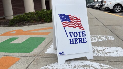 A white sandwich-style poster says "VOTE HERE" with an image of an American flag.