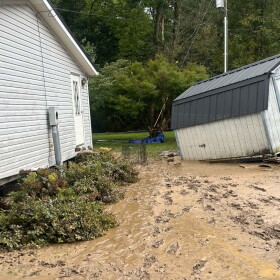 A storage shed that has been knocked over by flood waters sits in a muddy yard.