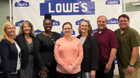 A group of people smiling in front of a Lowe's backdrop.