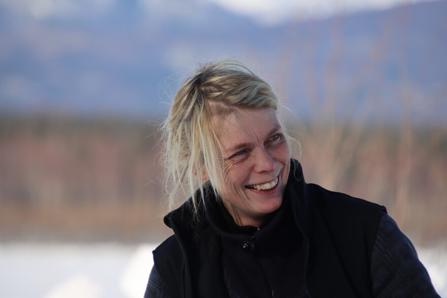 A blond woman smiles in front of some trees