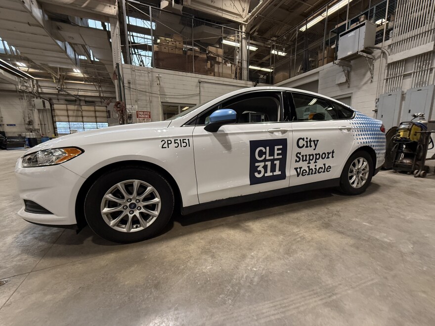 Cleveland's new 311 support vehicle, a mostly white sedan, sits in a city garage. The car is mounted with a camera and equipped with AI software.