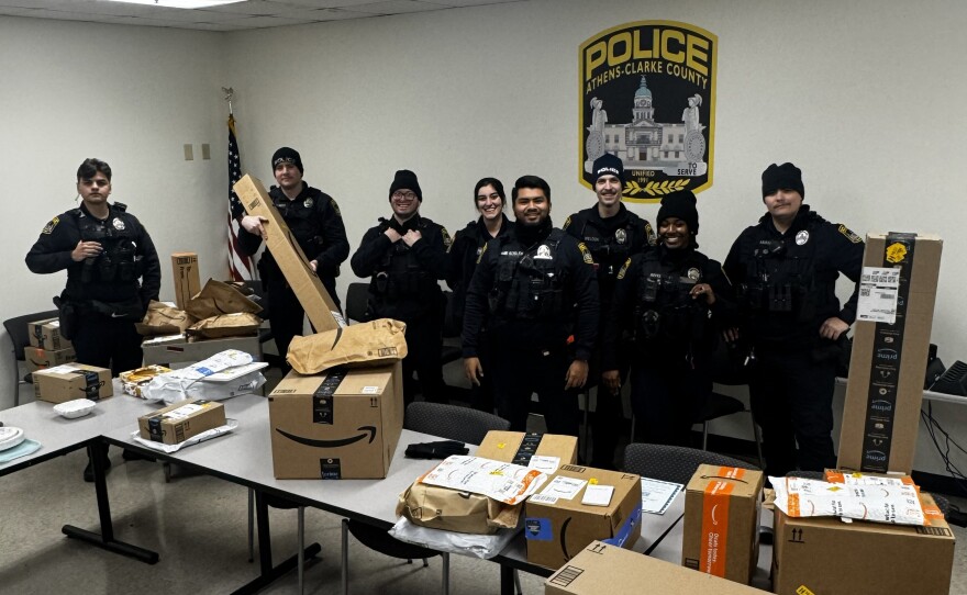 A group of Athens-Clarke County police officers stands behind tables filled with dozens of recovered Amazon packages.