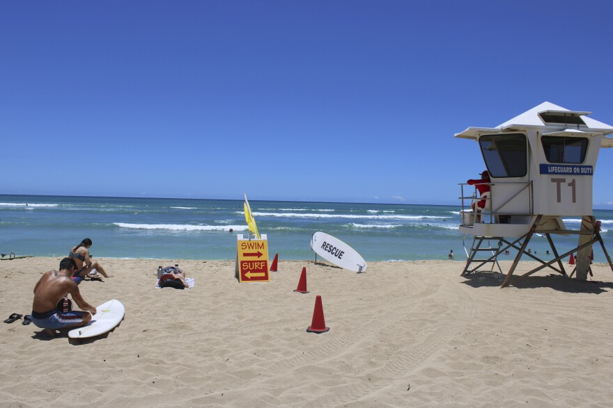 A surfer waxes his board in the sand at White Plains on May 12, 2023.