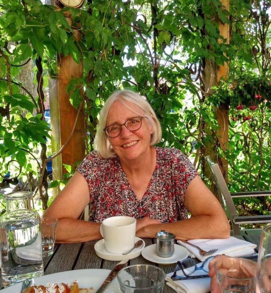 A woman sits at an outdoor cafe enjoying dessert and coffee, with a smile.