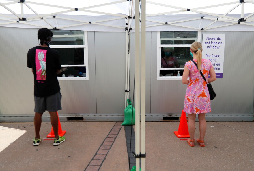 Parkland Memorial Hospital employees give instructions to a man and a woman on how to self-administer a test for the coronavirus at a Dallas walk-up facility. Texas saw a surge in cases within the past week.