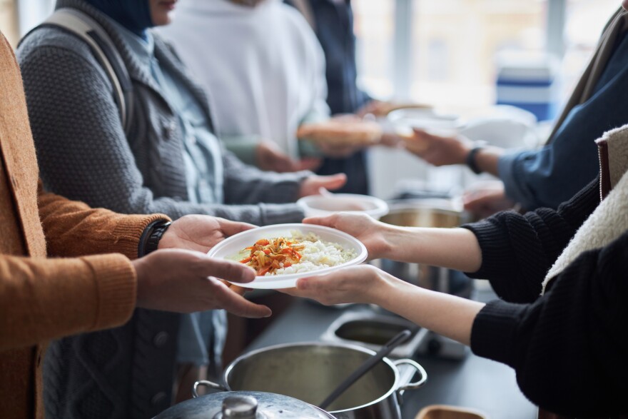 Side view closeup of unrecognizable volunteer giving hot meals to refugees in line at help center with focus on hands holding plate of rice