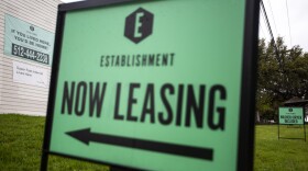 A green sign that says "Now Leasing" with an arrow pointing toward a white building in the background.