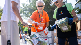 Dos mujeres cargan alimentos en un carrito de compras en un punto de distribución de alimentos móvil.