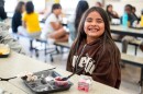 A girl looks at the camera with a big smile with plate with fruit and other food items