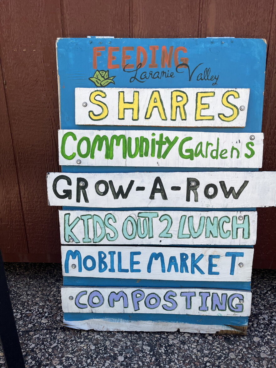 Colorful sign listing program offerings of a food program including "shares" "grow-a-row" and "composting"
