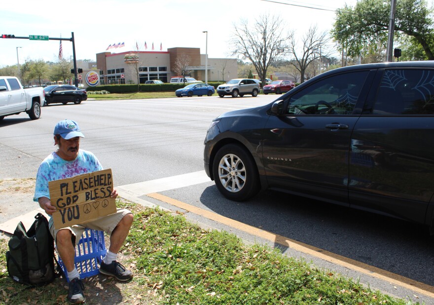 Ramine Dehgan panhandles at Northwest 62nd street and State Road 26 by The Oaks Mall in Gainesville. The grassy median there is more than 6 feet wide, so he can occupy it despite the new ordinance. (Lillian Lawson/WUFT News)