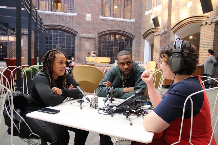 Two women and a man sitting at a table with microphones