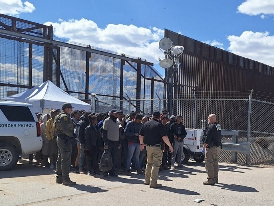 A group of several dozen migrants in El Paso who turned themselves in to U.S. Border Patrol officials on Thursday wait to be transported for processing after being detained.