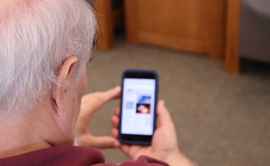 An older man looking at a library website on his smartphone.