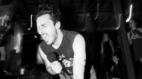Sal from Gatto Black on his knees, singing passionately into a microphone in a black and white photo.