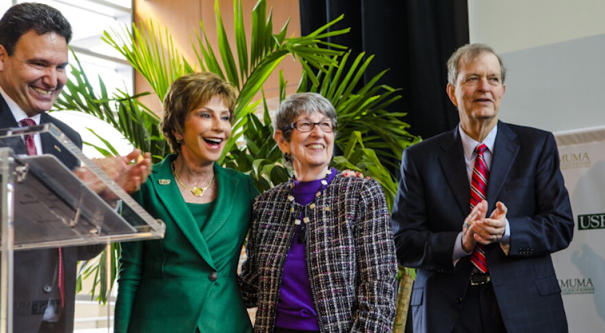 Four people - two men and two women - smile as they stand on a stage in front of a palm plant.