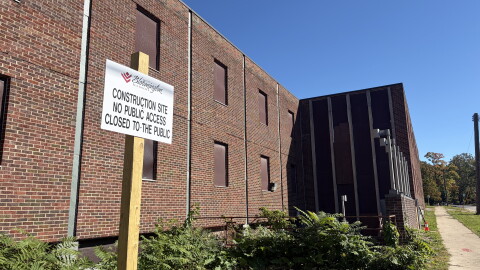 a sign on a wooden post sits in front of a brown brick building