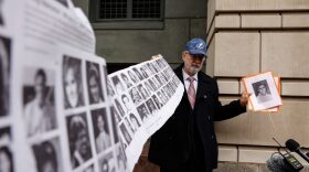 Paul Hudson, whose daughter Melina was one of the victims in the Pan Am Flight 103 Lockerbie bombing, holds up a banner of pictures of additional victims outside the federal court before the trial for a Libyan man accused of making the bomb that exploded the plane.