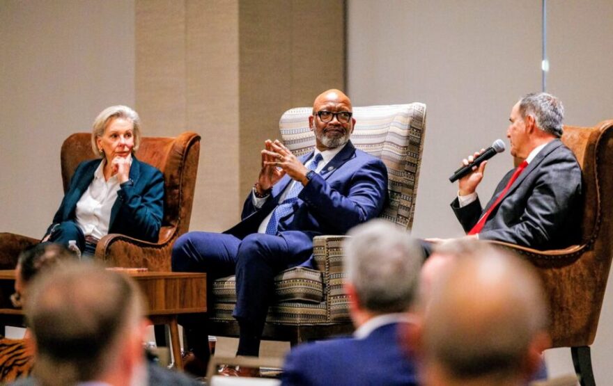 A woman and two men sit in large chairs 