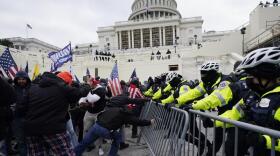 Rioters wearing mostly black push against a police barrier as Capitol police try to hold it in place.