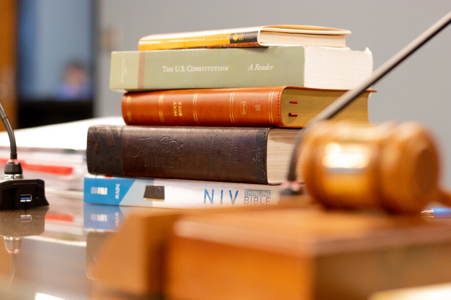 A stack of books, including three Bibles, sits on the table beside State Superintendent Ryan Walters at the June 2024 State Board of Education meeting.