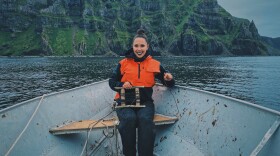 A woman rowing a boat with mountains behind her.
