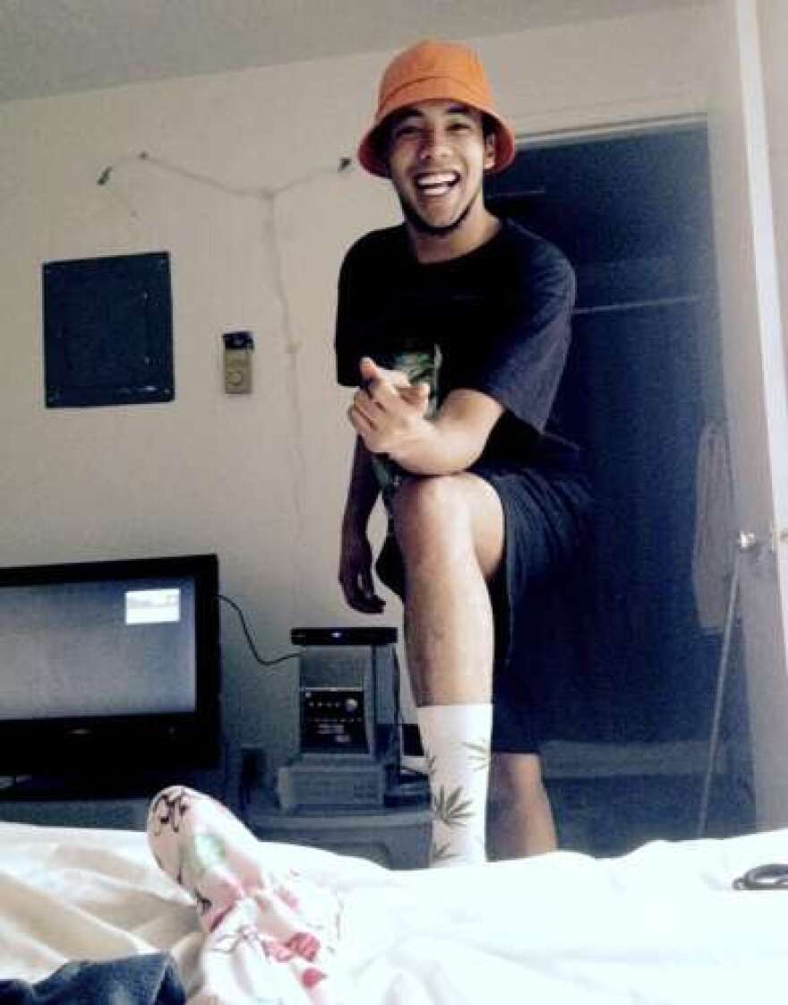 Young man in orange hat in a bedroom with TV in background.