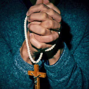 Two hands hold a slim white rope with a dangling wooden cross.