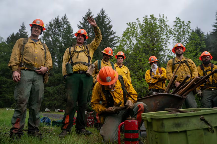 People in firefighter gear gather around another person with equipment.
