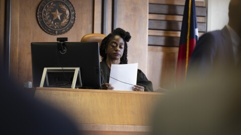 A woman wearing a judge's robe looks at a photo at her desk.