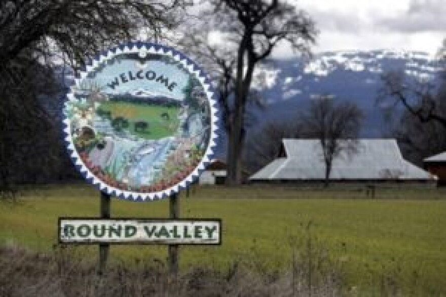  A sign reads Welcome Round Valley. Barns and a snow-covered mountain in the background.