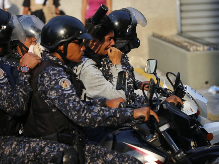 A detained anti-government protester is driven away on a motorcycle by National Police during clashes between protesters and security forces in Caracas on Wednesday.