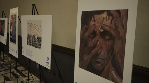 A painting of a hand partially covering a man's face as the painting hangs in a conference center display next to a row of other pieces of artwork