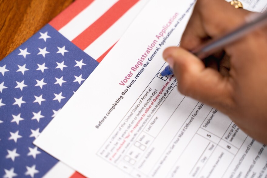 Close up of a hand holding a pen and writing on a form titled Voter Registration Application