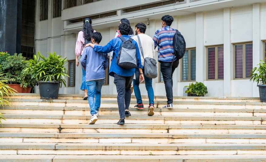 Back view shot of students with backpacks walking up steps on campus