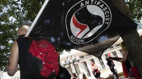A person holds a black flag that says "ANTIFASCIST ACTION"