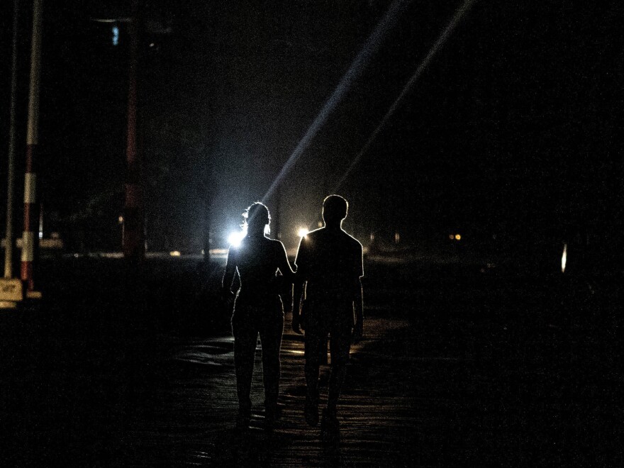 A couple walks down the middle of a street in the dark during a blackout in Havana, Cuba, Wednesday, Sept. 28, 2022.