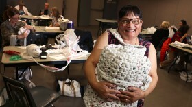 Merri Medley holding one of her finished mats as volunteers work in the background