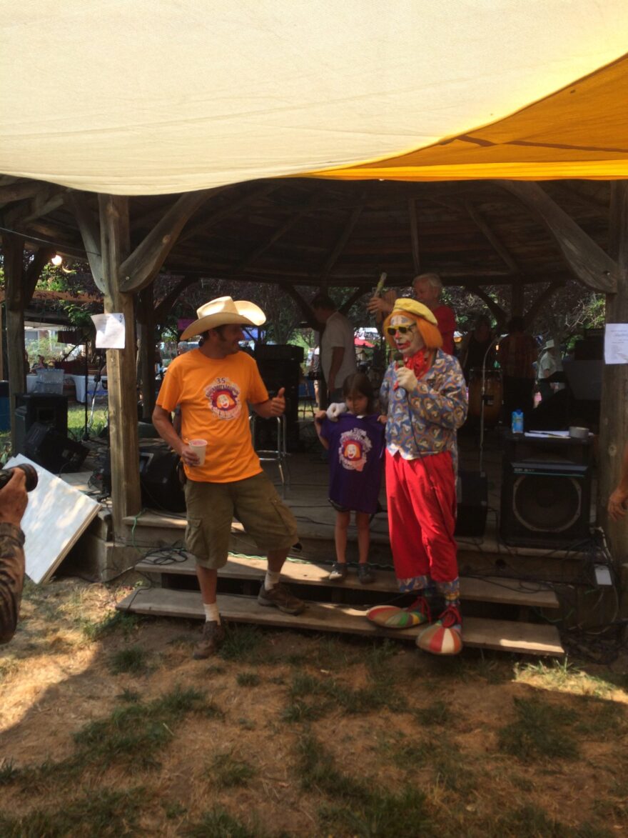 A clown stands with a child and a man wearing a cowboy hat.