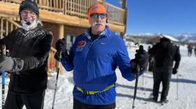 A man in ski gear and sunglasses holding ski poles.