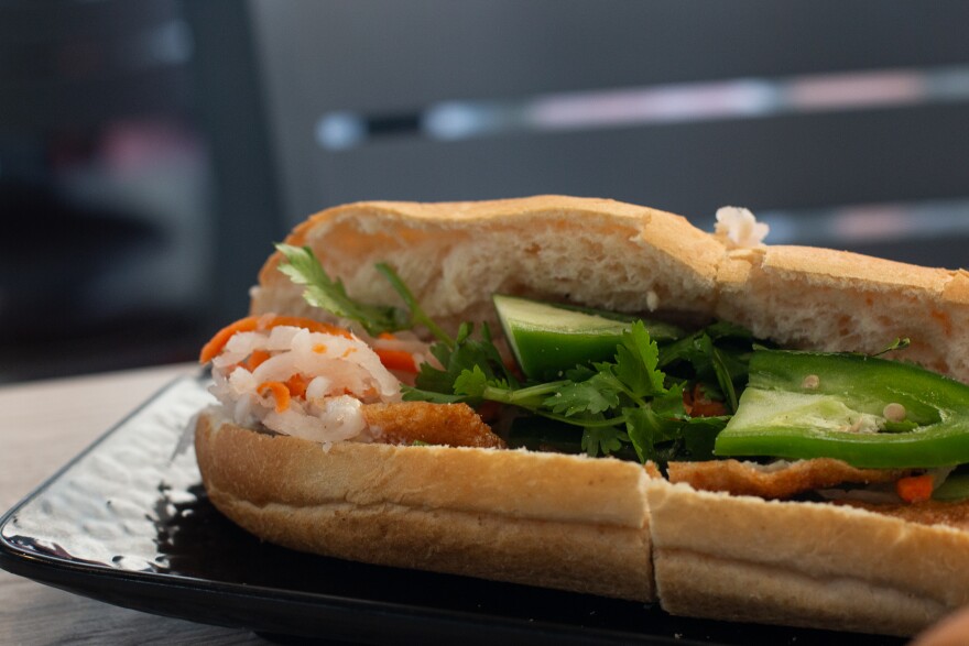 A full bahn mi sandwich sits on a black plate