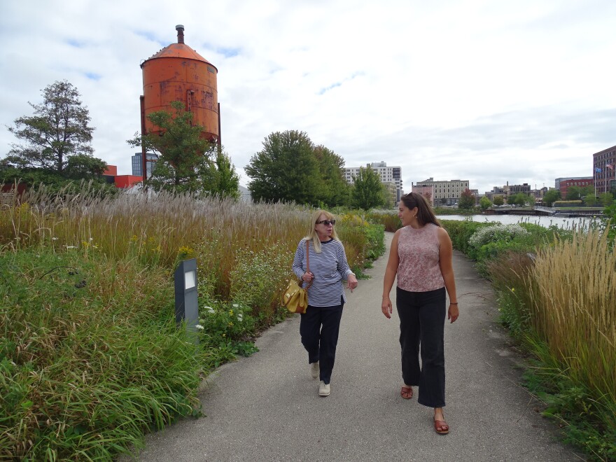 Woman standing next to a light post that has the Water Current Walking Tour sign.