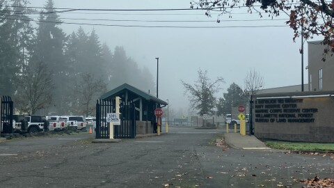 An entrance to a government facility. There is a guard house and a stop sign. 