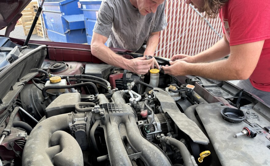 Two volunteers replace headlights on a vehicle at the light repair clinic, Aug. 4, 2026.