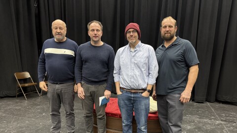 Four men standing on stage with a black curtain behind them.